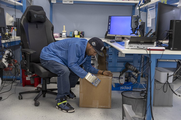 An employee packaging and preparing electronic components for shipping, using tape.