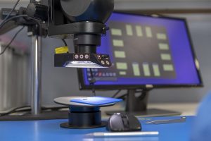 Desk with a PC monitor and a close-up view of a microscope used for quality testing electronic components.