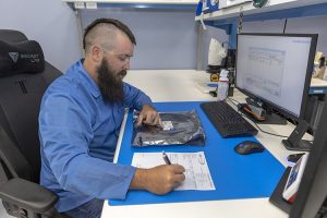 An employee at AGS Devices preparing a document for components shipment at his desk, with a PC, in a close-up view.