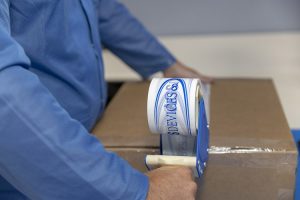 Close-up of a man taping a package with electronic components, preparing them for shipping.