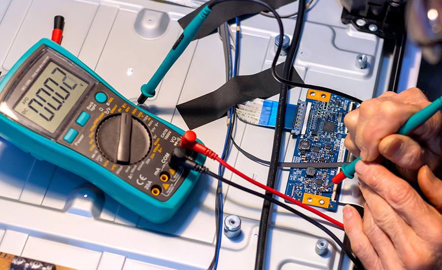 A man using a multimeter to test a small circuit board on a table.